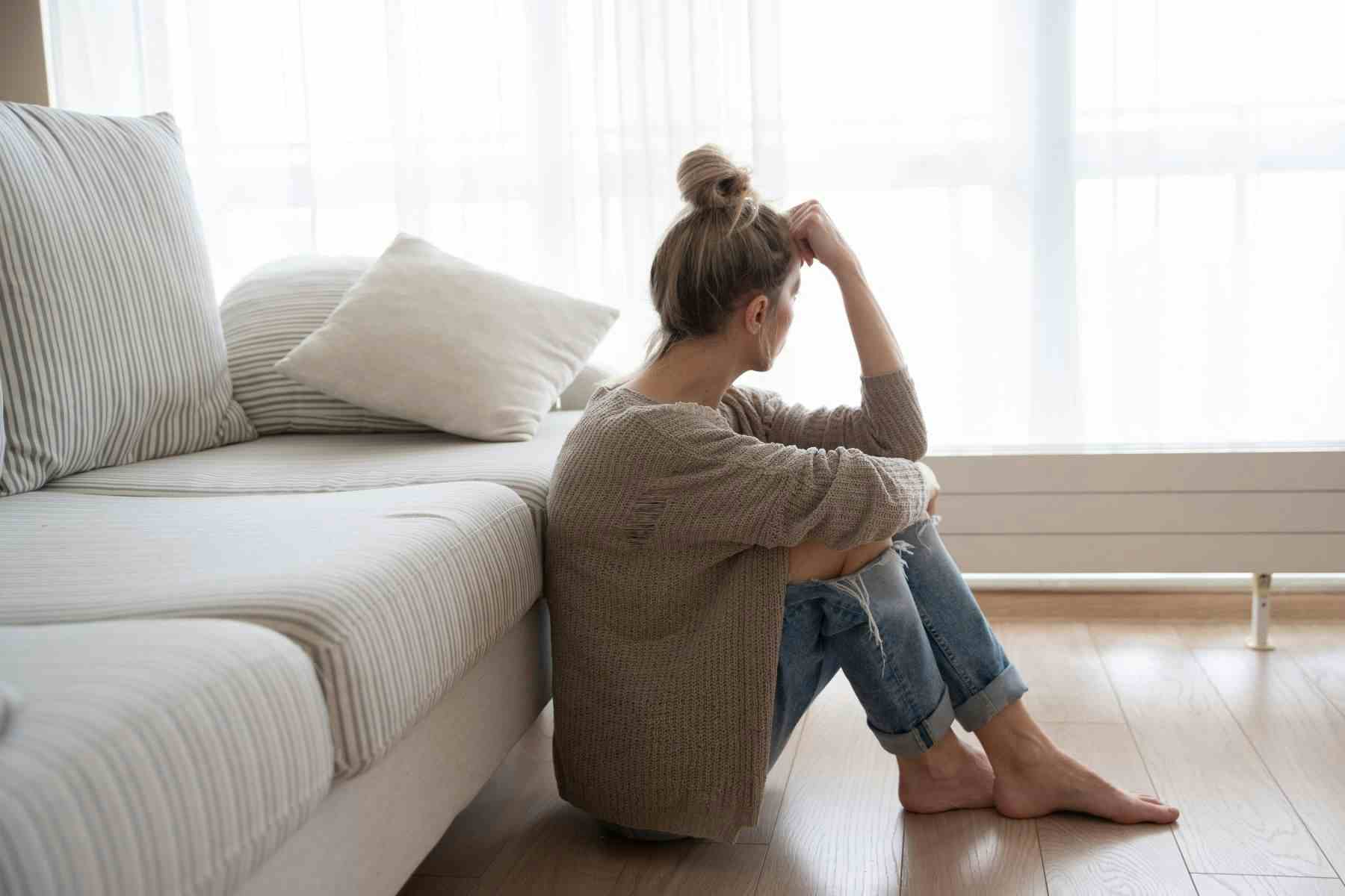 Depressed woman sitting on living room floor